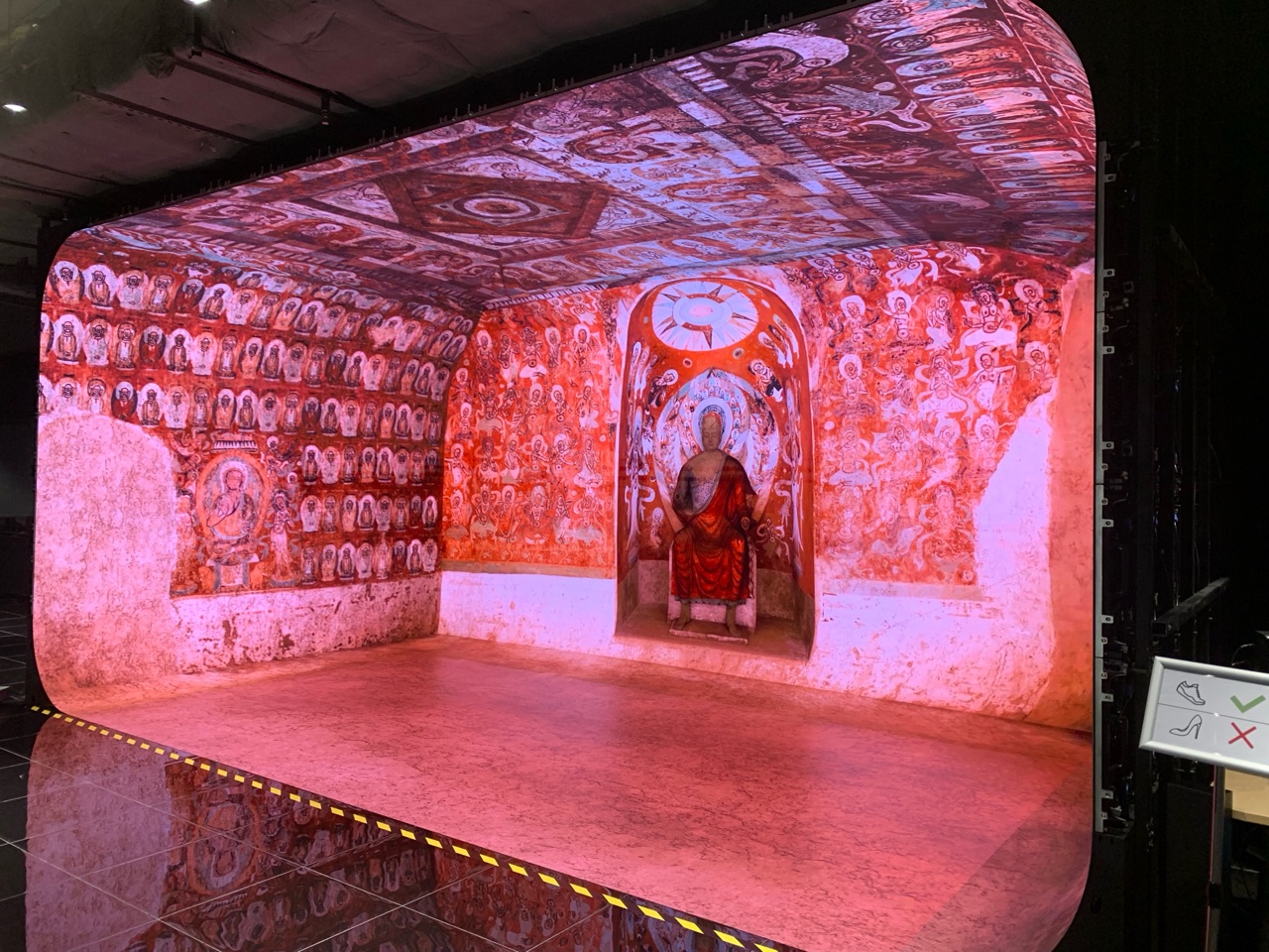 Inside the immersive projection cave, warm red tones recreate Dunhuang cave murals, thousand Buddha figures, and a central niche.